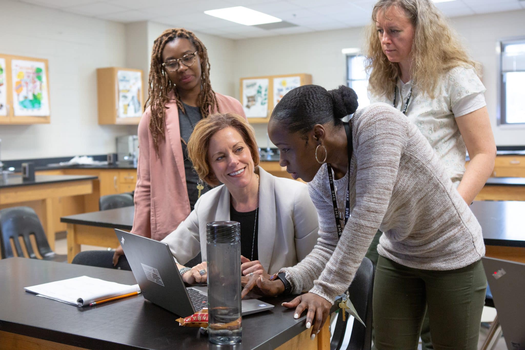 A group of educators working together. One teacher sits at a desk while three others stand around her.