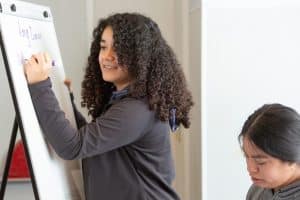 A student writes her answer on a whiteboard during a lesson in precalculus class.