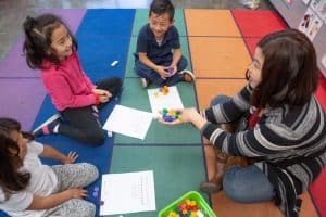 A kindergarten teacher uses number cubes during a small-group math activity.