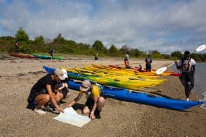 students at lake looking at map and working with canoes