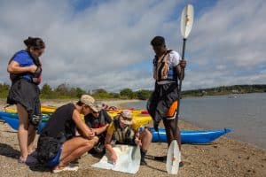 students and staff looking at map on lake with canoe gear