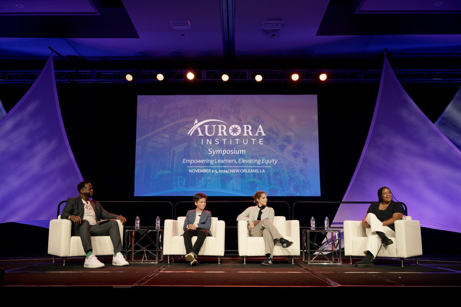 Carlos Moreno and three students on stage at the Aurora Institute Symposium 2024