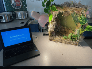 A laptop open next to a small project covered in fake greenery. 