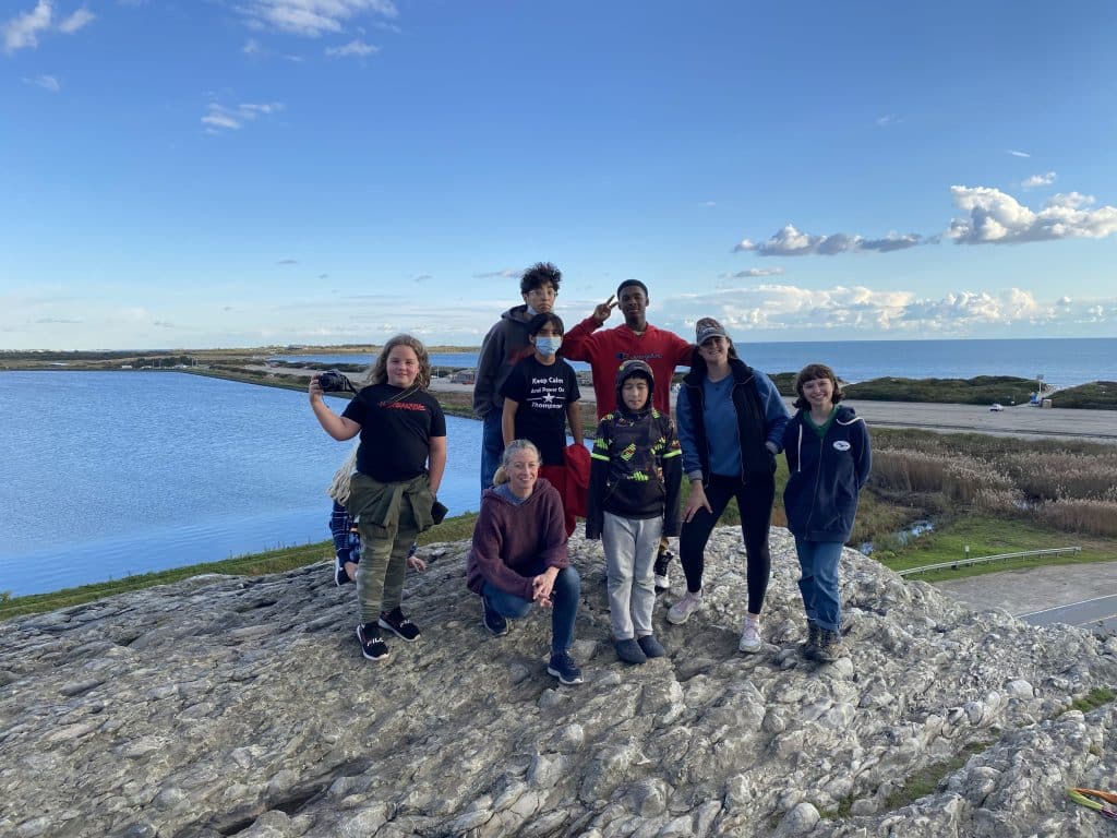 Students and a teacher stand on top of a cliff smiling.