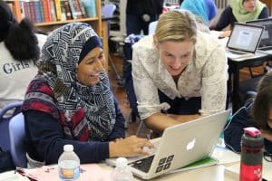 Student and educator in classroom looking at laptop while smiling