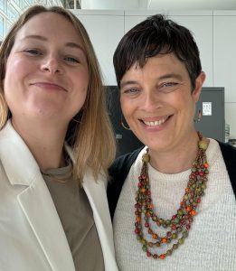 Two women smiling at the camera, both wearing white tops.