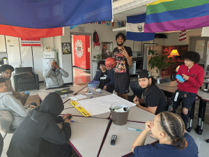 students gather around a table in a room with various colorful flags displayed