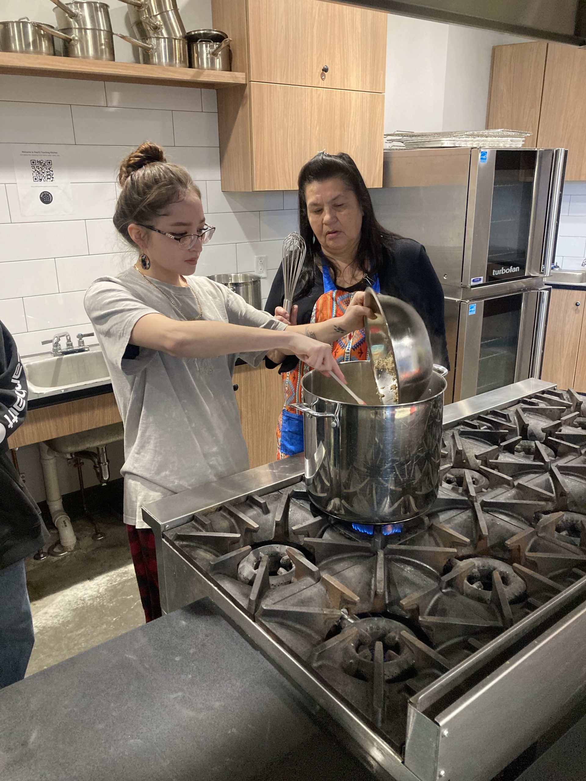 Hands-on competency-based learning in action in a kitchen where a student is being mentored by an elder