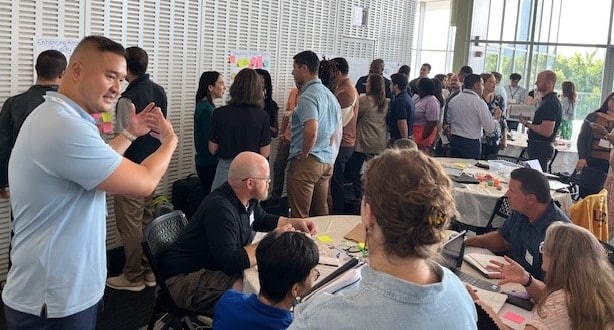 A room of people talking and adding post-it notes to a wall